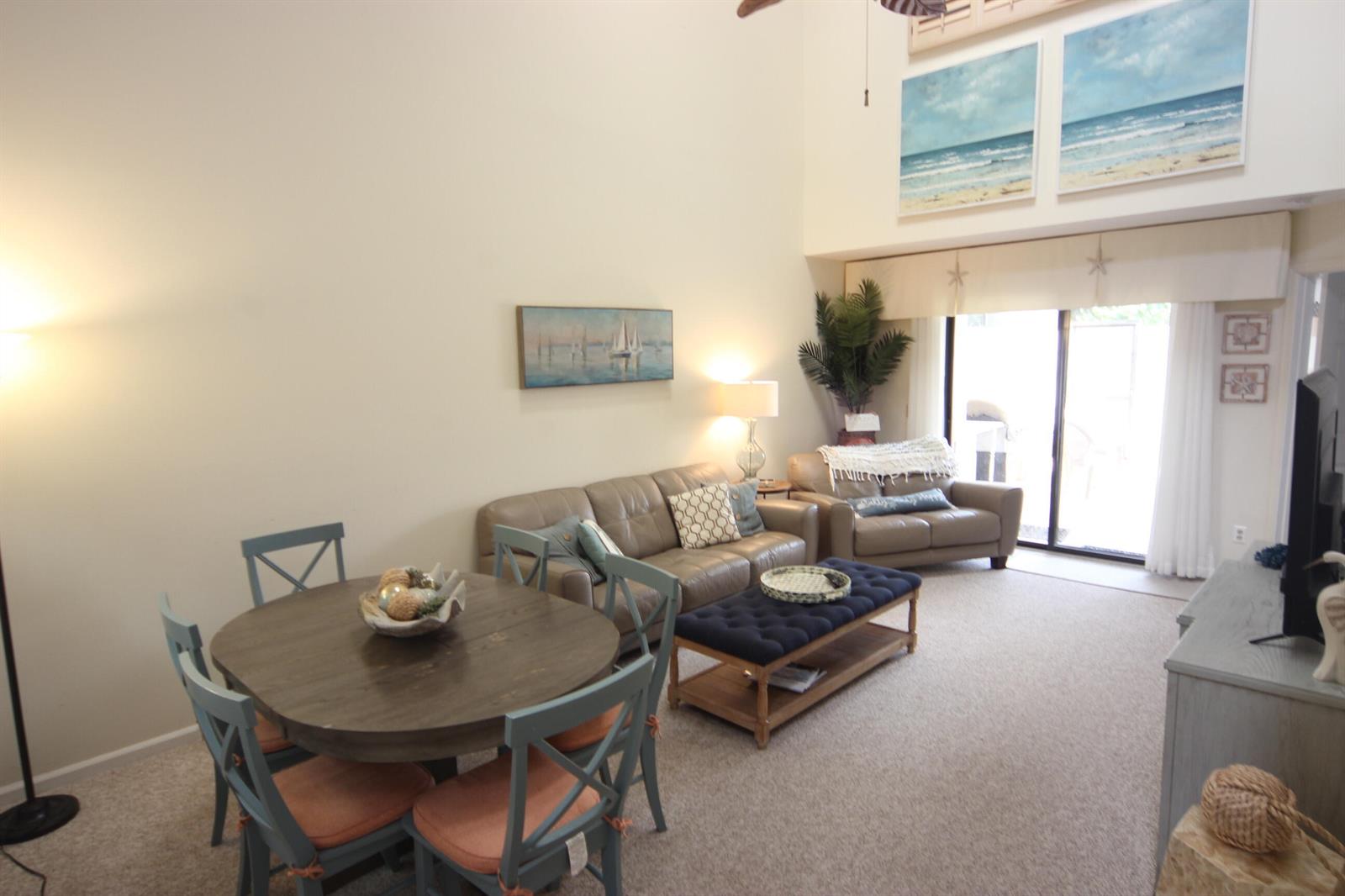 A living and dining area features vaulted ceilings, beige carpet, and coastal-themed wall art — 508 Sea Oats Drive # 4, Juno Beach FL 33408, JUNO BEACH, FL