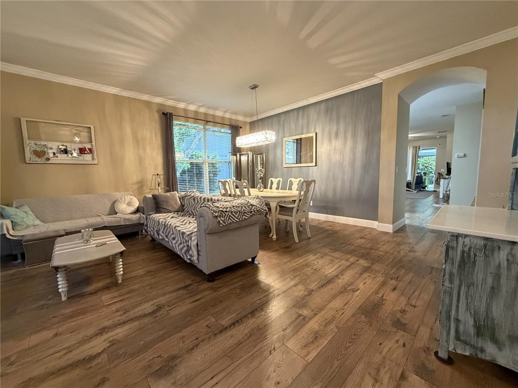 An open-concept living and dining area features wood-look flooring and a gray accent wall — 923 BRIDGEWAY BOULEVARD, ORLANDO, FL