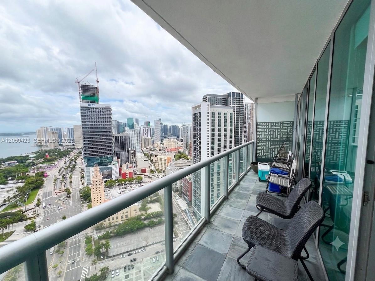A balcony with gray tile flooring overlooks a city skyline and a large body of water — 888 Biscayne Blvd # 4005, Miami FL 33132, MIAMI, FL