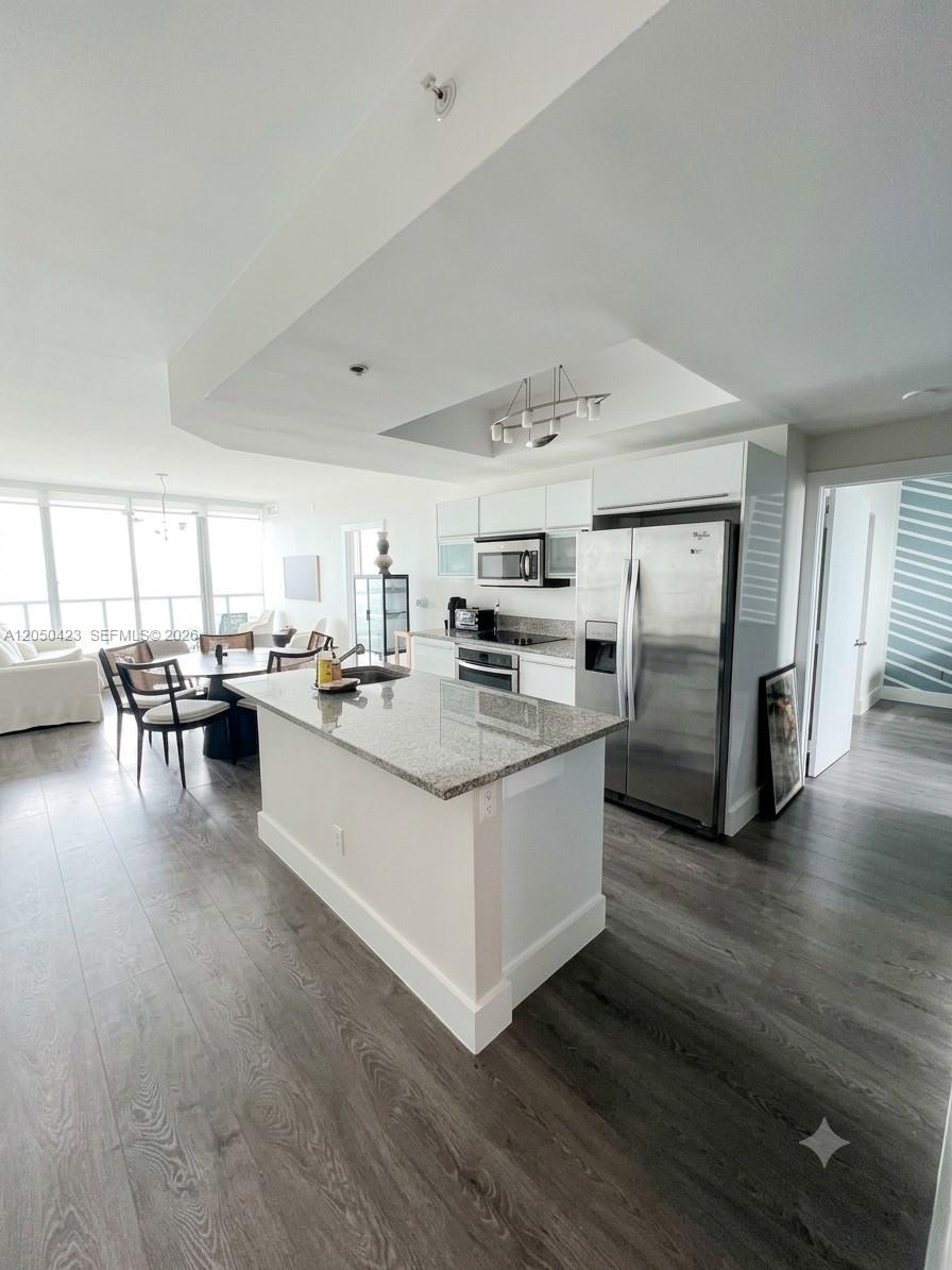 A modern kitchen features a granite-topped island, stainless steel appliances, and dark wood-look flooring — 888 Biscayne Blvd # 4005, Miami FL 33132, MIAMI, FL