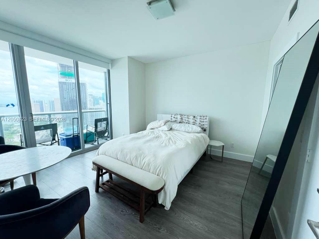 A bedroom features a bed with a bench, a floor mirror, and floor-to-ceiling windows — 888 Biscayne Blvd # 4005, Miami FL 33132, MIAMI, FL
