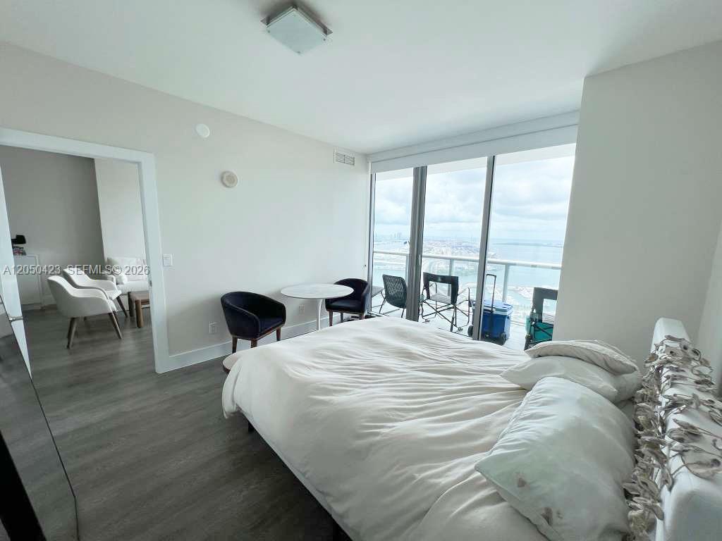 A bedroom features a white bed, a small dining set, and floor-to-ceiling windows with balcony access — 888 Biscayne Blvd # 4005, Miami FL 33132, MIAMI, FL