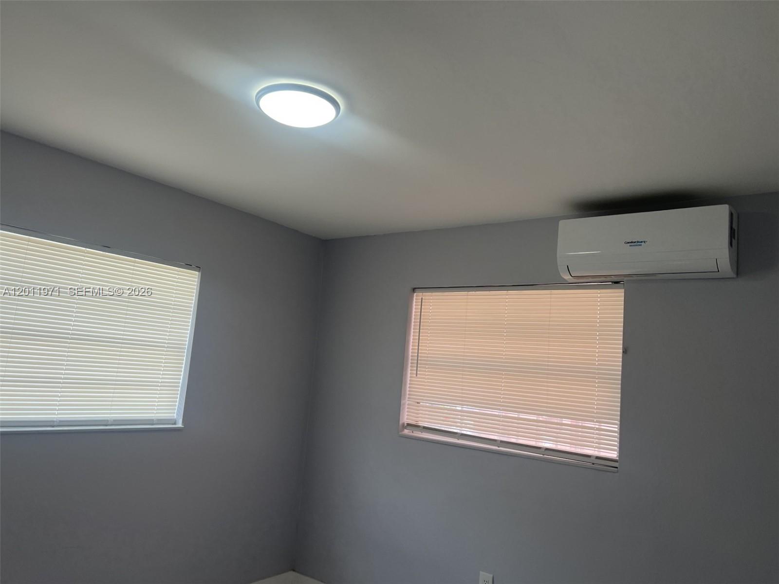 A room with gray walls, two windows with blinds, a ceiling light, and a wall-mounted AC — 1067 NW 24th St # 1067, Miami FL 33127, MIAMI, FL