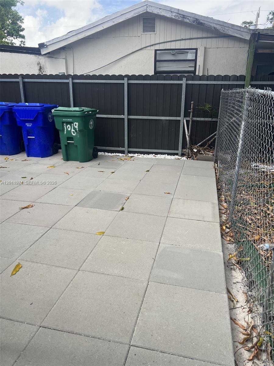 A paved patio area features two trash bins against a dark fence and chain-link fencing — 1067 NW 24th St # 1067, Miami FL 33127, MIAMI, FL