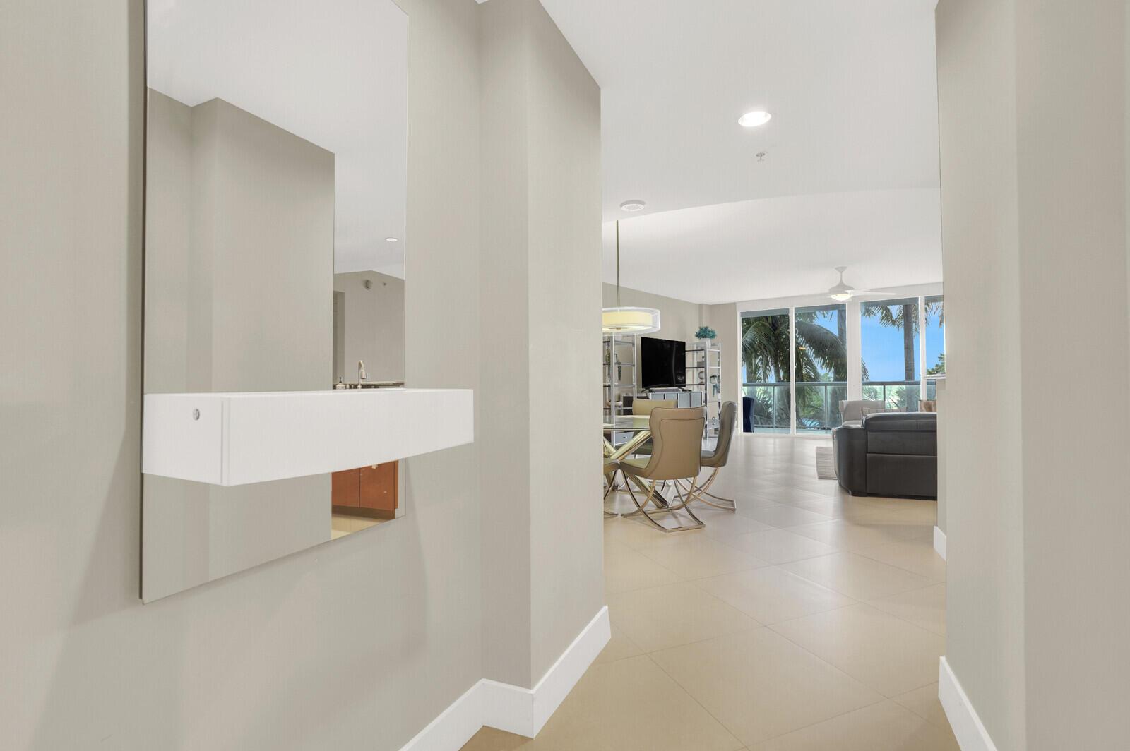 A hallway with a wall-mounted mirror and shelf leads into an open-concept living and dining area — 1 N Ocean Boulevard # 508, Pompano Beach FL 33062, POMPANO BEACH, FL