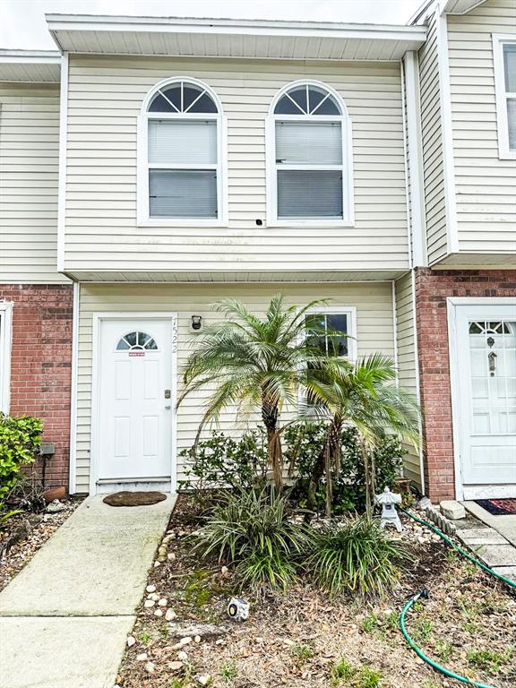 A two-story townhouse exterior features light siding, arched windows, and a small front garden — 7522 HOLLOWELL DRIVE, TAMPA, FL