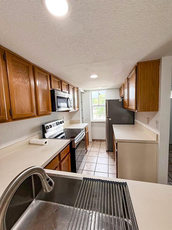 A kitchen features wood cabinets, white countertops, stainless steel appliances, and tile flooring — 7522 HOLLOWELL DRIVE, TAMPA, FL