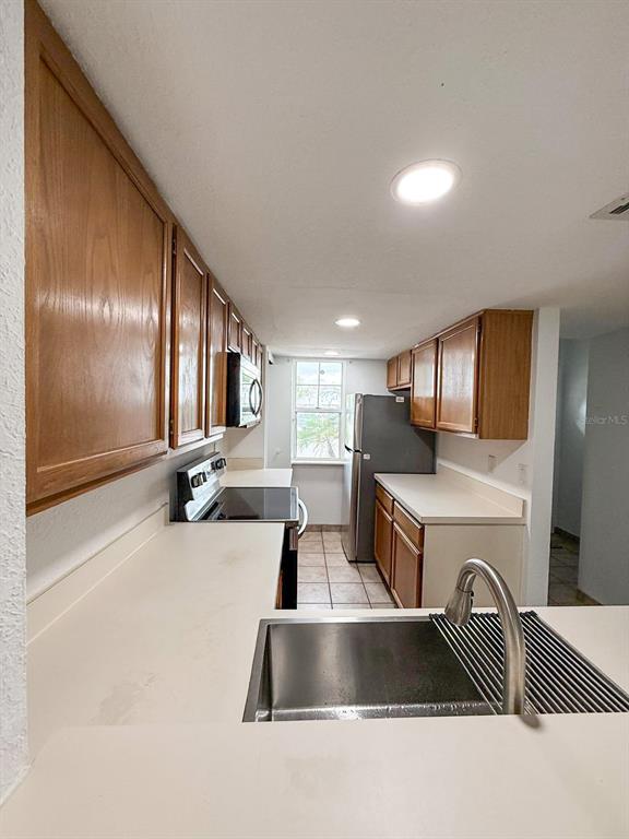 A kitchen features wooden cabinets, white countertops, stainless steel appliances, and a tiled floor — 7522 HOLLOWELL DRIVE, TAMPA, FL