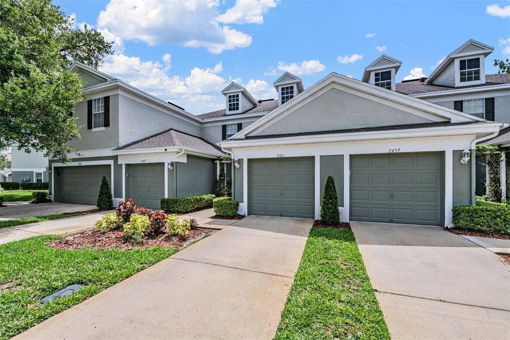 A multi-unit residential building features gray stucco siding, green garage doors, and multiple dormer windows — 2461 EARLSWOOD COURT, BRANDON, FL