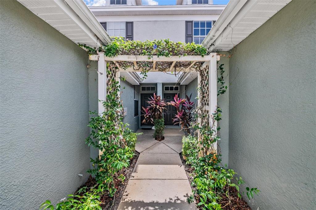 A concrete walkway leads through a wooden trellis covered in vines to two front doors — 2461 EARLSWOOD COURT, BRANDON, FL