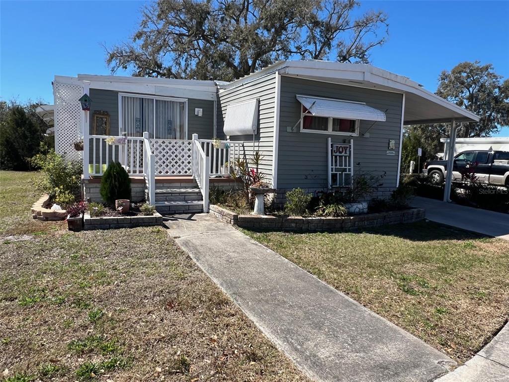 A gray mobile home features a front porch, a concrete walkway, and a carport — 29250 US HIGHWAY 19 N UNIT 300, CLEARWATER, FL