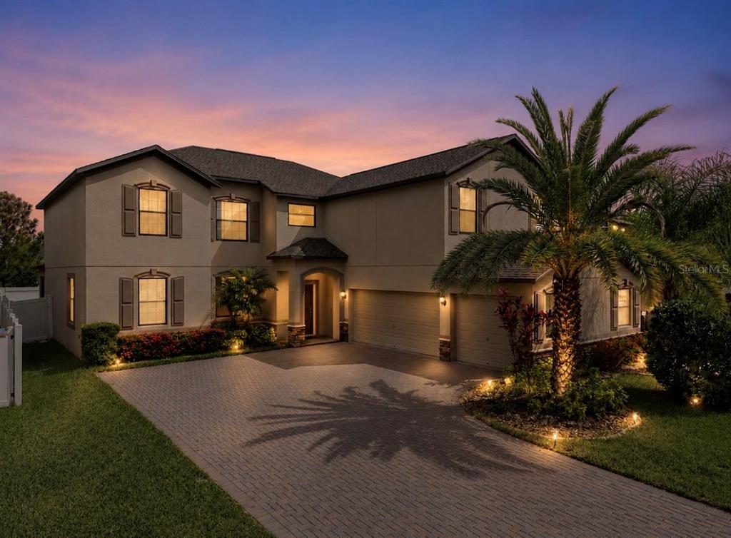 A two-story house with a paved driveway, a palm tree, and exterior lighting at dusk — 9924 SMARTY JONES DRIVE, RUSKIN, FL