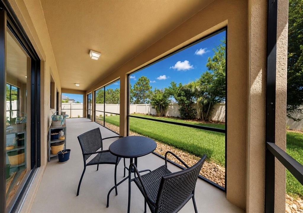 A covered screened-in patio features a small bistro set and views of a fenced backyard — 9924 SMARTY JONES DRIVE, RUSKIN, FL