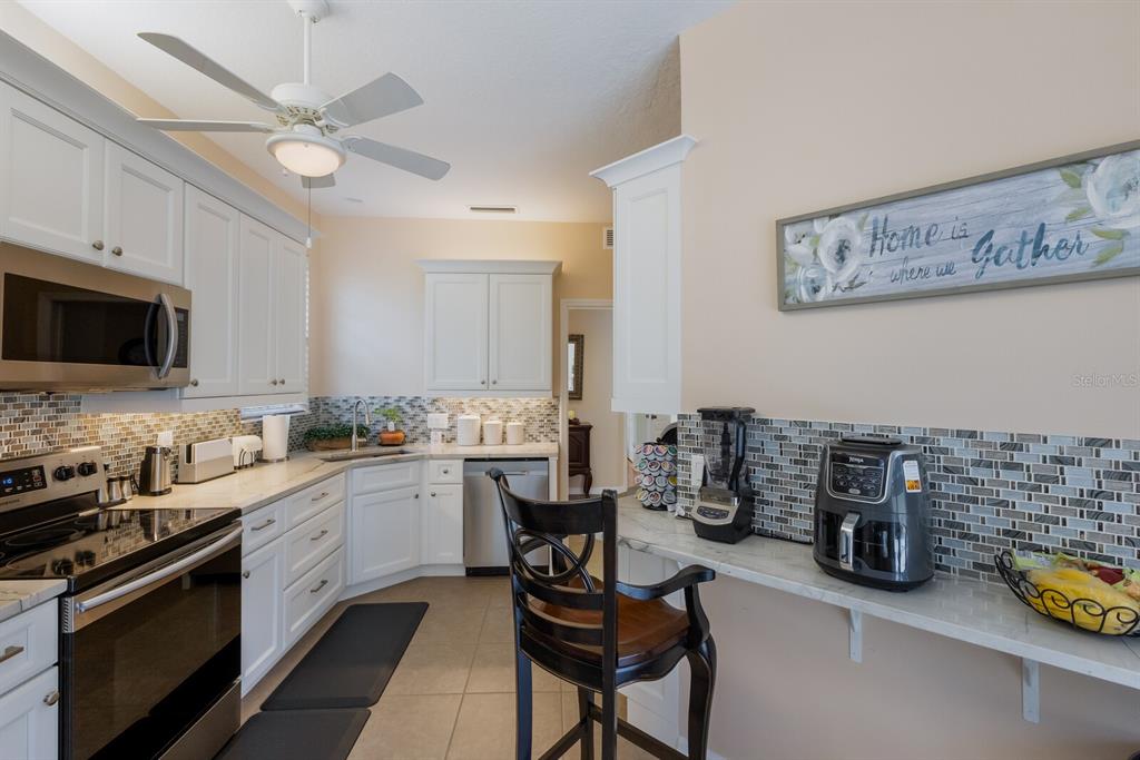 A kitchen features white cabinets, stainless steel appliances, a tiled backsplash, and a breakfast bar — 915 SW BARCLAY COURT, VENICE, FL
