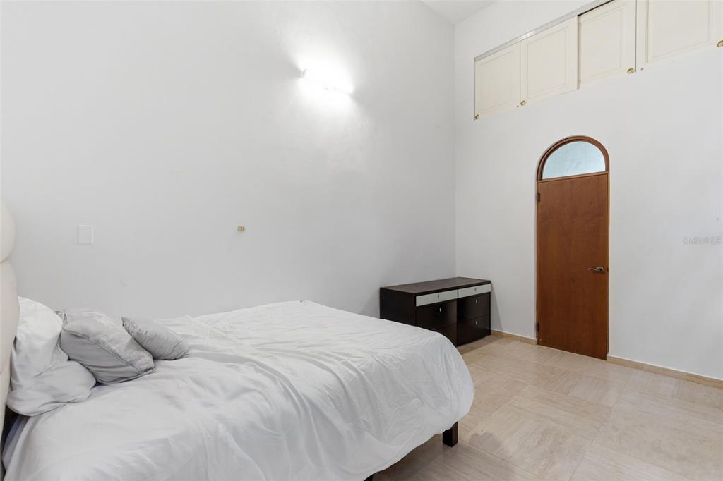 A bedroom features a bed, a dark dresser, a wooden arched door, and overhead storage cabinets — 65 CALLE SAN FRANCISCO, OLD SAN JUAN, PR