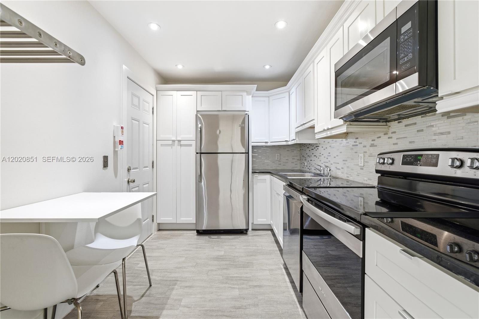 A kitchen features white cabinetry, stainless steel appliances, black countertops, and a small dining table — 1200 Mariposa Ave # E104, Coral Gables FL 33146, CORAL GABLES, FL