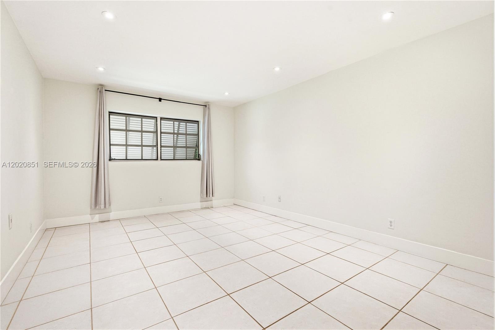 An empty room with white walls, light-colored tile flooring, and a window with curtains — 1200 Mariposa Ave # E104, Coral Gables FL 33146, CORAL GABLES, FL