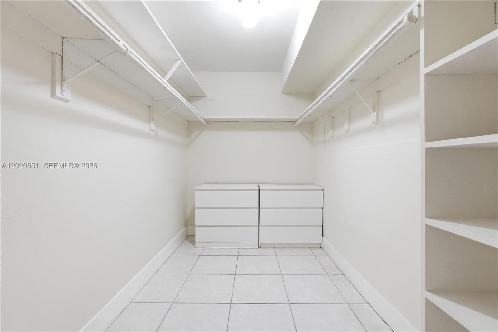 A walk-in closet features white walls, tile flooring, hanging rods, shelving, and two dressers — 1200 Mariposa Ave # E104, Coral Gables FL 33146, CORAL GABLES, FL