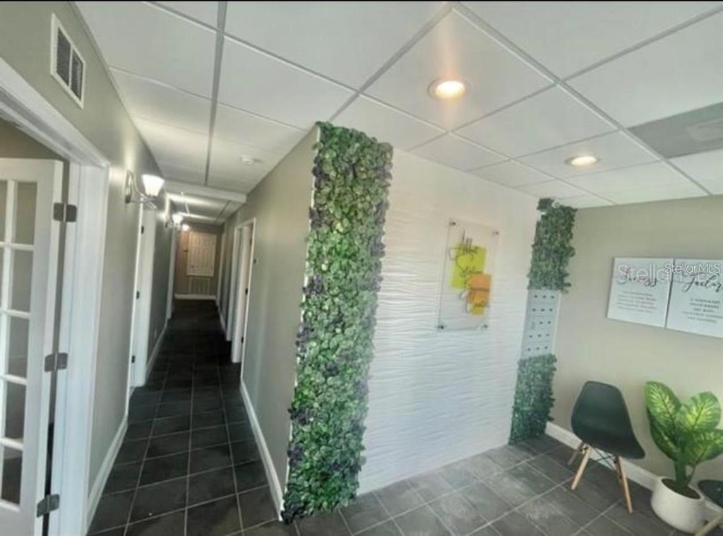 A hallway features dark tile flooring, a textured white accent wall, and vertical green plant panels — 6272 ABBOTT STATION DRIVE UNIT 101-20, ZEPHYRHILLS, FL