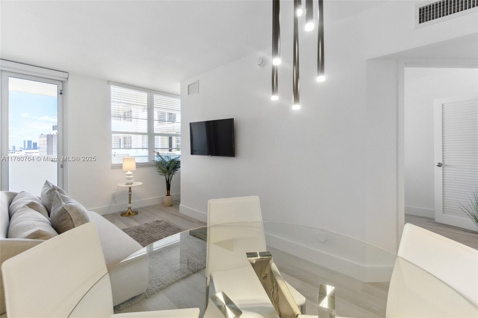 A modern living and dining area features white walls, light flooring, and a glass table — 100 Lincoln Rd # 1218, Miami Beach FL 33139, MIAMI BEACH, FL