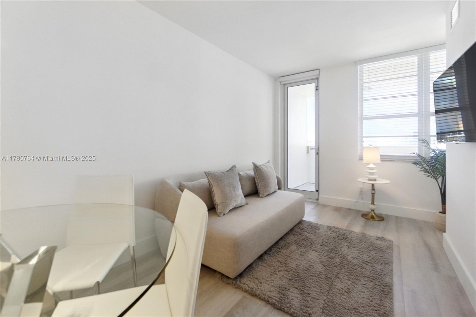 A living room features a beige sofa, a glass dining table, and a balcony door — 100 Lincoln Rd # 1218, Miami Beach FL 33139, MIAMI BEACH, FL