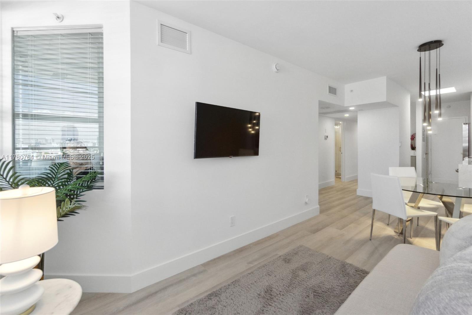 A modern living room features light wood flooring, a wall-mounted television, and a dining area — 100 Lincoln Rd # 1218, Miami Beach FL 33139, MIAMI BEACH, FL