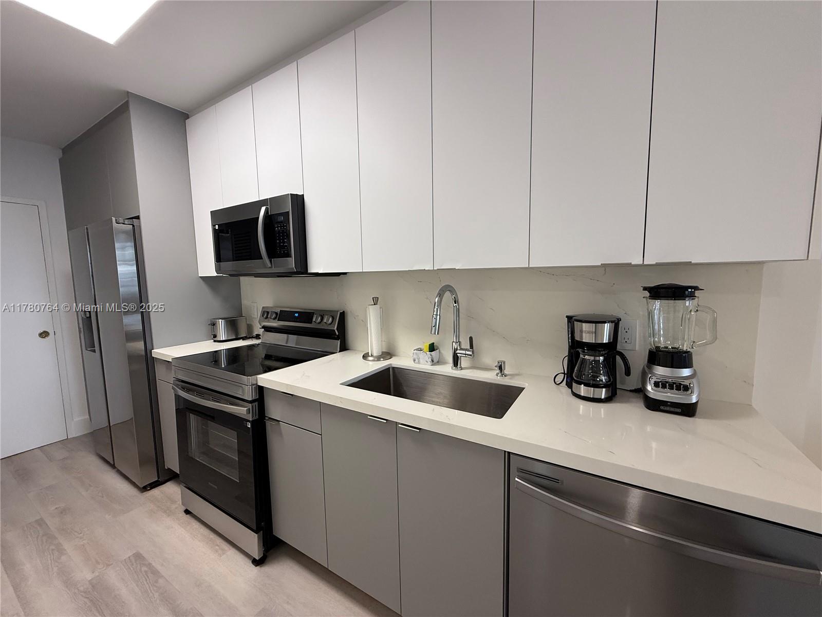 A modern kitchen features white upper cabinets, gray lower cabinets, stainless steel appliances, and countertops — 100 Lincoln Rd # 1218, Miami Beach FL 33139, MIAMI BEACH, FL