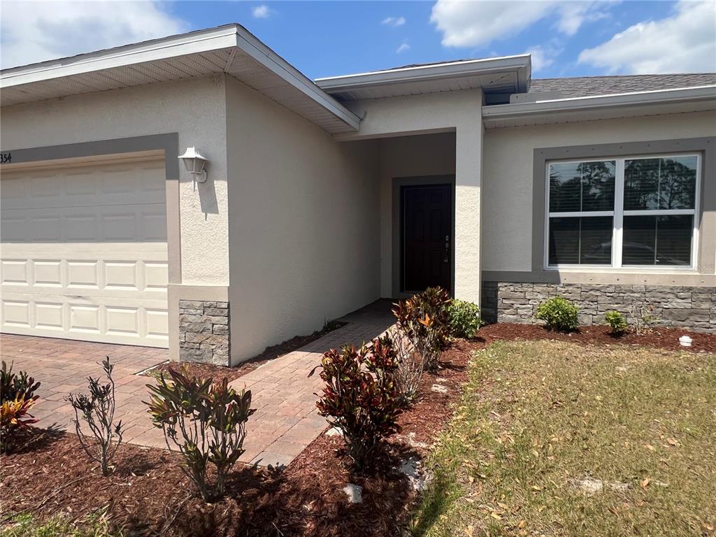 The exterior of a single-story house features a paved walkway, stone accents, and landscaping — 354 ALBATROSS ROAD, ROTONDA WEST, FL