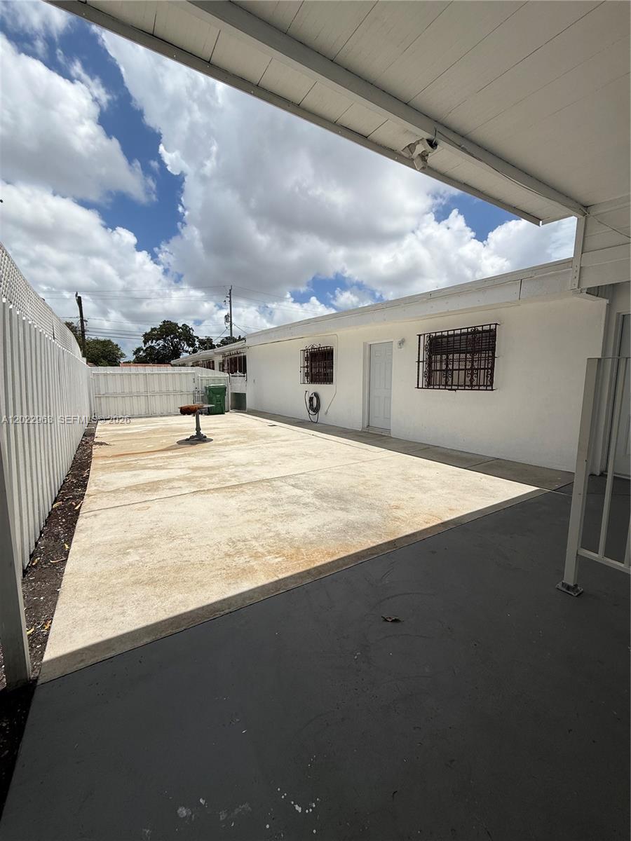 A concrete patio area sits beside a white house with barred windows under a roof — 1046 NW 33rd Ave, Miami FL 33125, MIAMI, FL