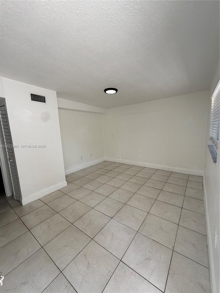An empty room features white walls, a tiled floor, and a single ceiling light fixture — 1046 NW 33rd Ave, Miami FL 33125, MIAMI, FL
