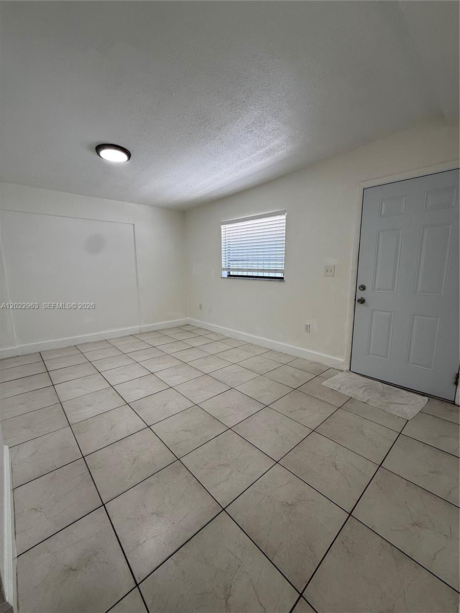 An empty room features white walls, a tiled floor, a window with blinds, and a door — 1046 NW 33rd Ave, Miami FL 33125, MIAMI, FL