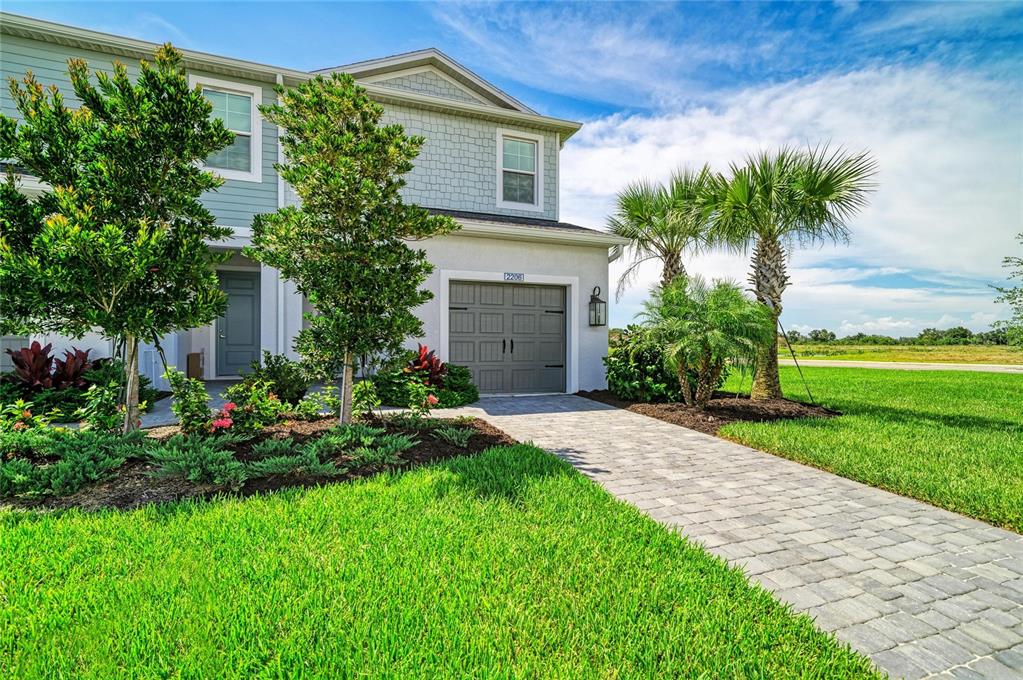 A two-story townhouse exterior features a gray garage, a paved walkway, and landscaping with palms — 2206 WASHINGTON PALM COURT, BRADENTON, FL