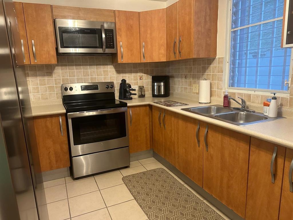 A kitchen features wood cabinets, stainless steel appliances, a tiled backsplash, and a double sink — 1 SUNBAY MARINA VILLAS, FAJARDO, PR