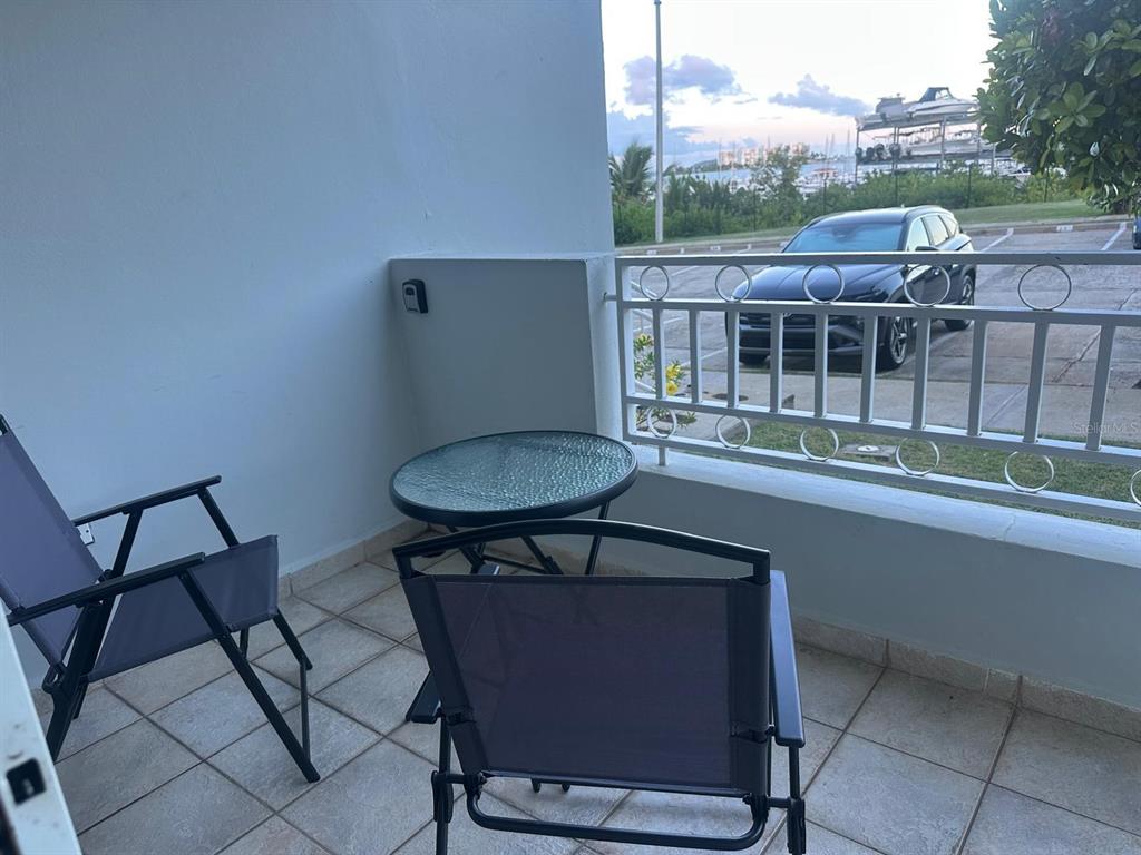 A balcony features two chairs, a small glass table, and a metal railing overlooking parking — 1 SUNBAY MARINA VILLAS, FAJARDO, PR