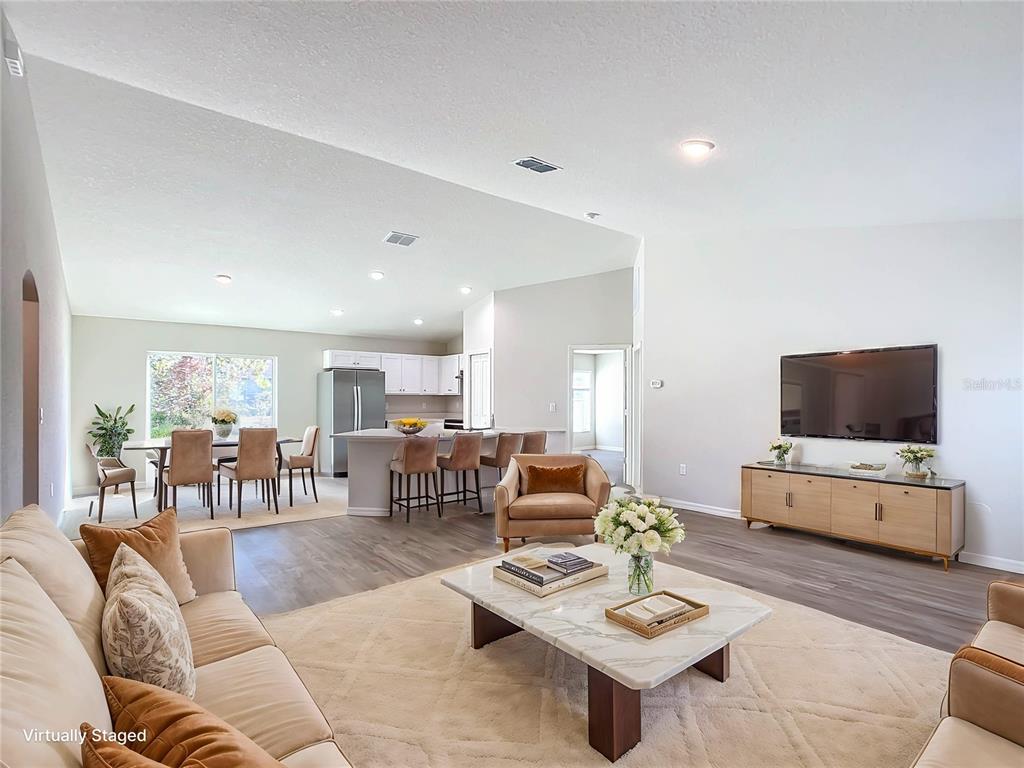 An open-concept living room and kitchen area with light flooring and vaulted ceilings — 12063 SE 89TH AVENUE, BELLEVIEW, FL