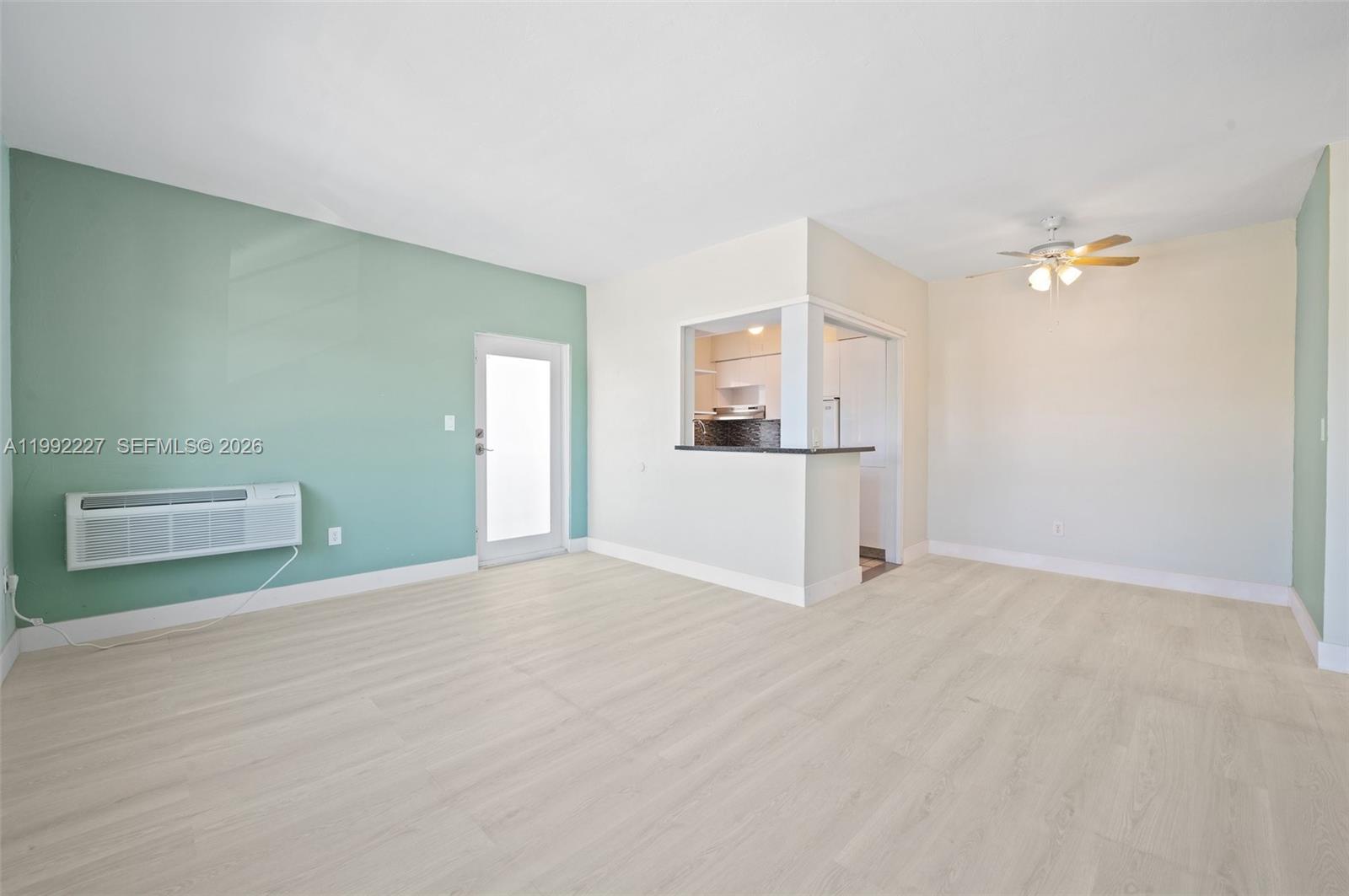 An empty living room features light wood-look flooring, a teal accent wall, and a kitchen pass-through — 7315 Byron Ave # 10, Miami Beach FL 33141, MIAMI BEACH, FL