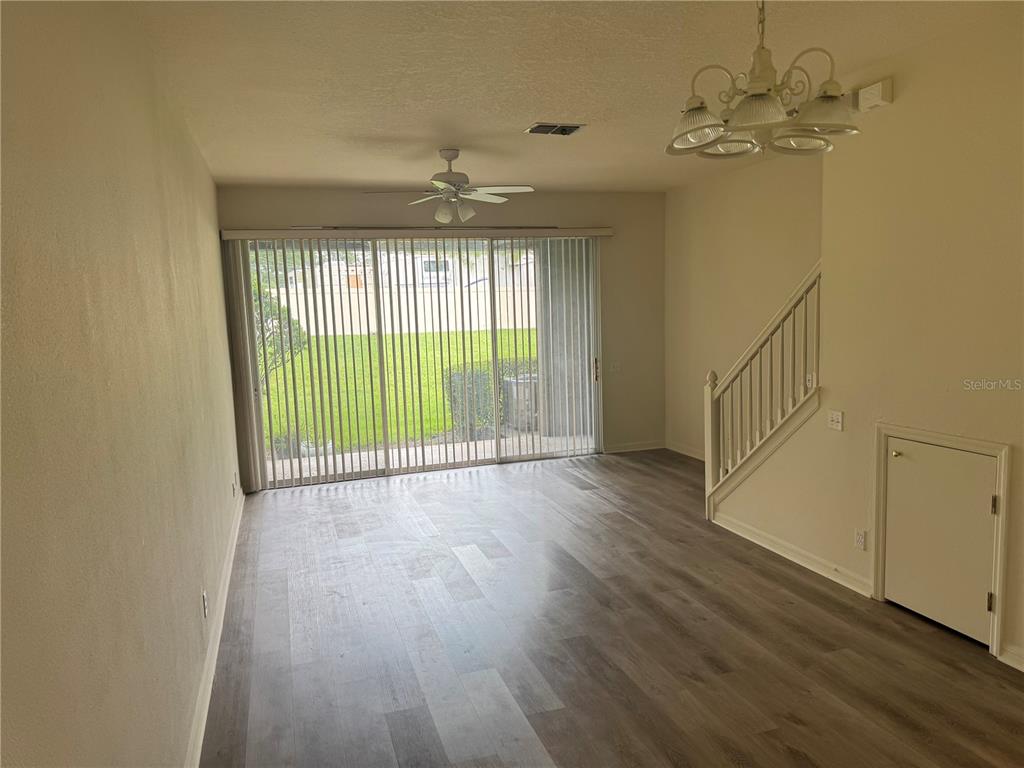 An empty room features wood-look flooring, a ceiling fan, a staircase, and sliding glass doors — 4133 KEY THATCH DRIVE, TAMPA, FL