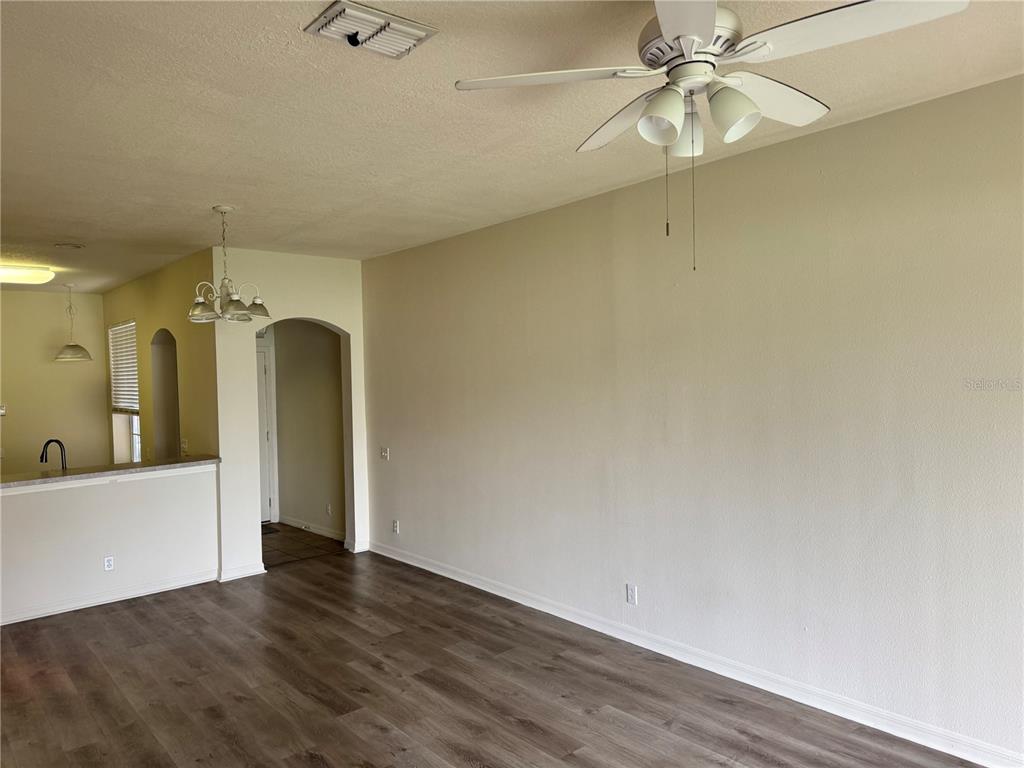 A living room with wood-look flooring, a ceiling fan, and an adjacent kitchen area — 4133 KEY THATCH DRIVE, TAMPA, FL