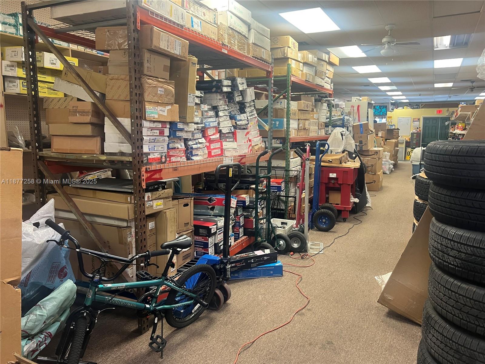 A cluttered storage room features metal shelving units filled with boxes, a bicycle, and stacked tires — LAUDERDALE LAKES, FL