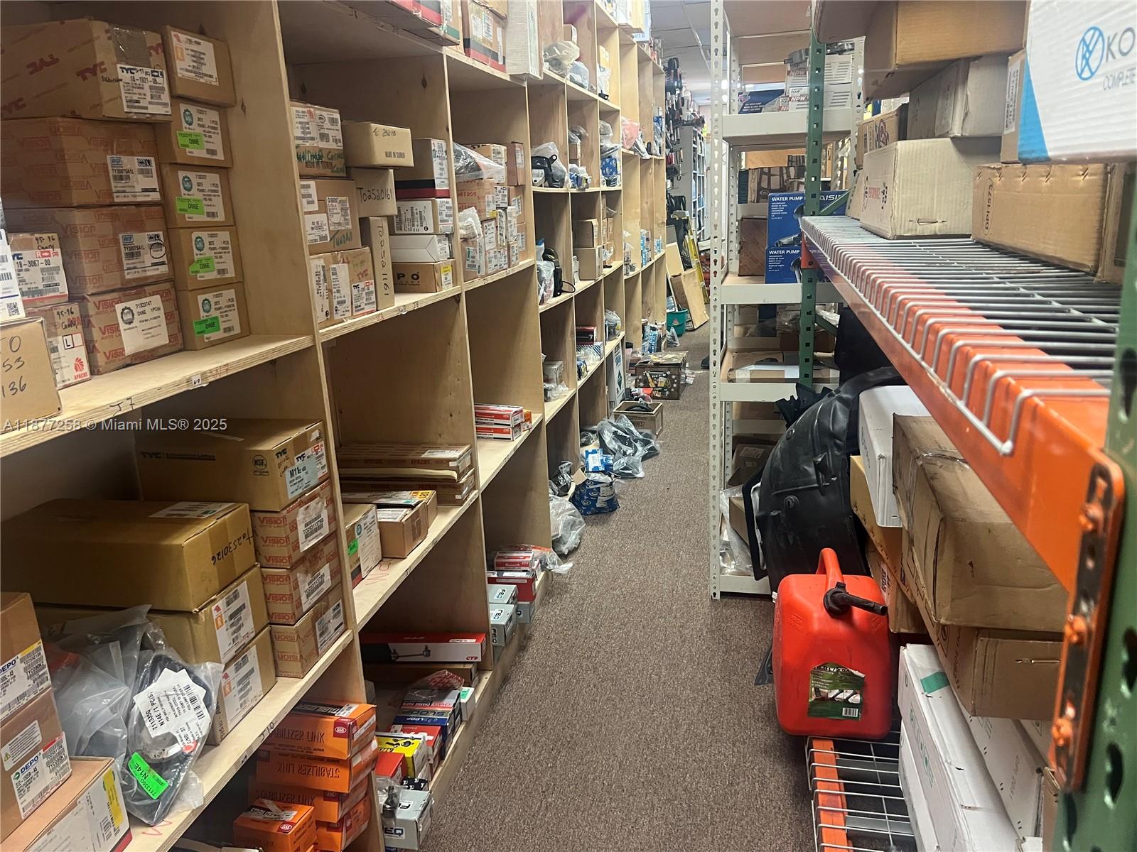 A narrow storage aisle features wooden shelving units filled with various boxed automotive parts — LAUDERDALE LAKES, FL