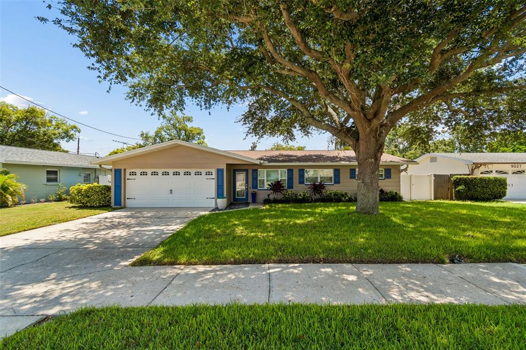 A single-story house with a white garage door, tan siding, and a large front tree — 9045 RIDGE ROAD, SEMINOLE, FL