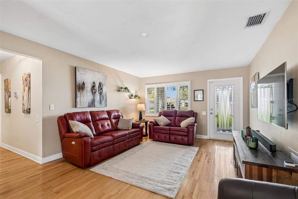 A living room features two red leather sofas, a wooden media console, and hardwood floors — 9045 RIDGE ROAD, SEMINOLE, FL