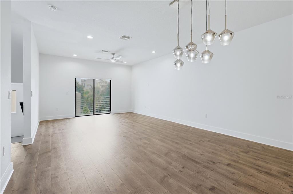 A bright, empty room features light wood-look flooring, white walls, and a modern glass chandelier — 2551 11TH PL N, ST PETERSBURG, FL
