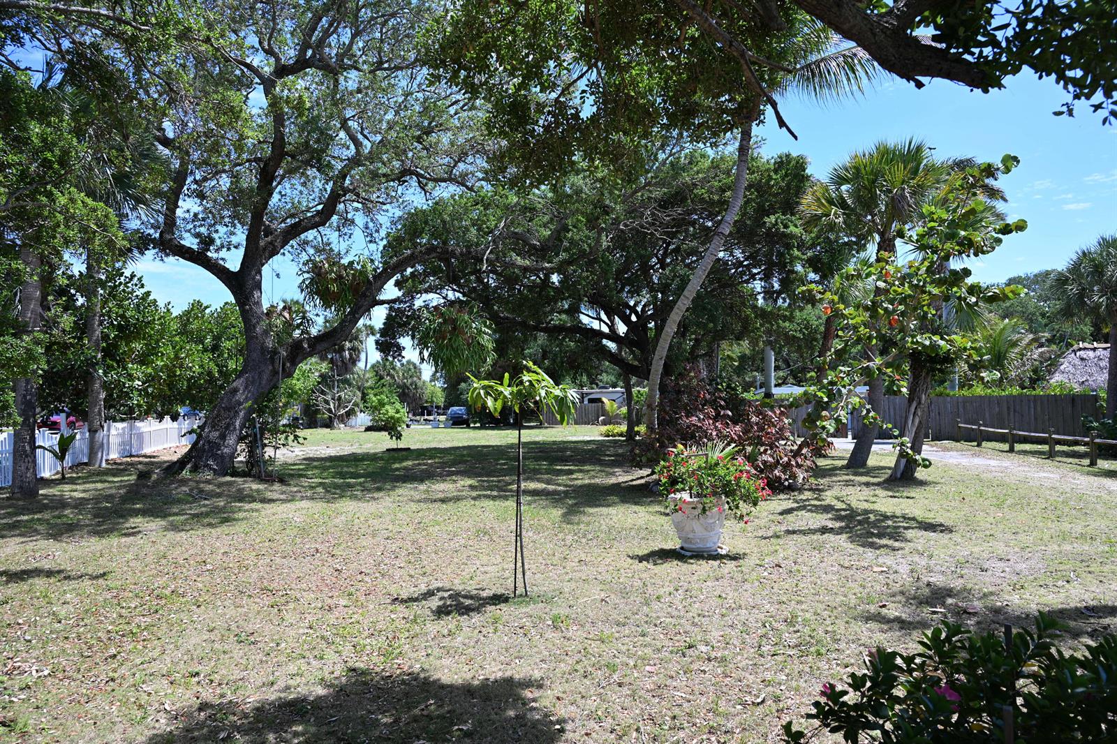 A grassy backyard features large oak trees, a potted plant, and a white picket fence — 18019 N Highway A1a, Jupiter FL 33477, JUPITER, FL