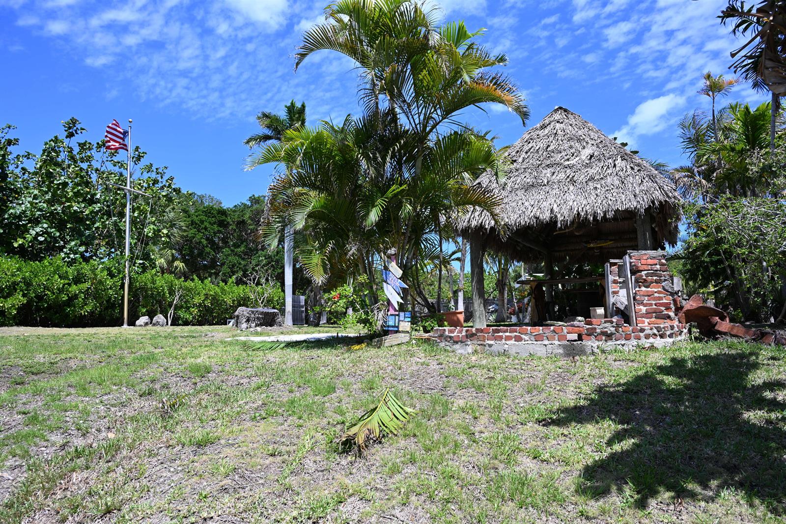 A thatched-roof tiki hut stands in a grassy yard next to a tall flagpole — 18019 N Highway A1a, Jupiter FL 33477, JUPITER, FL
