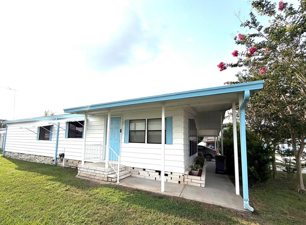 A white mobile home features a light blue door, matching shutters, and a covered carport — 3937 CHRIS DRIVE, WESLEY CHAPEL, FL