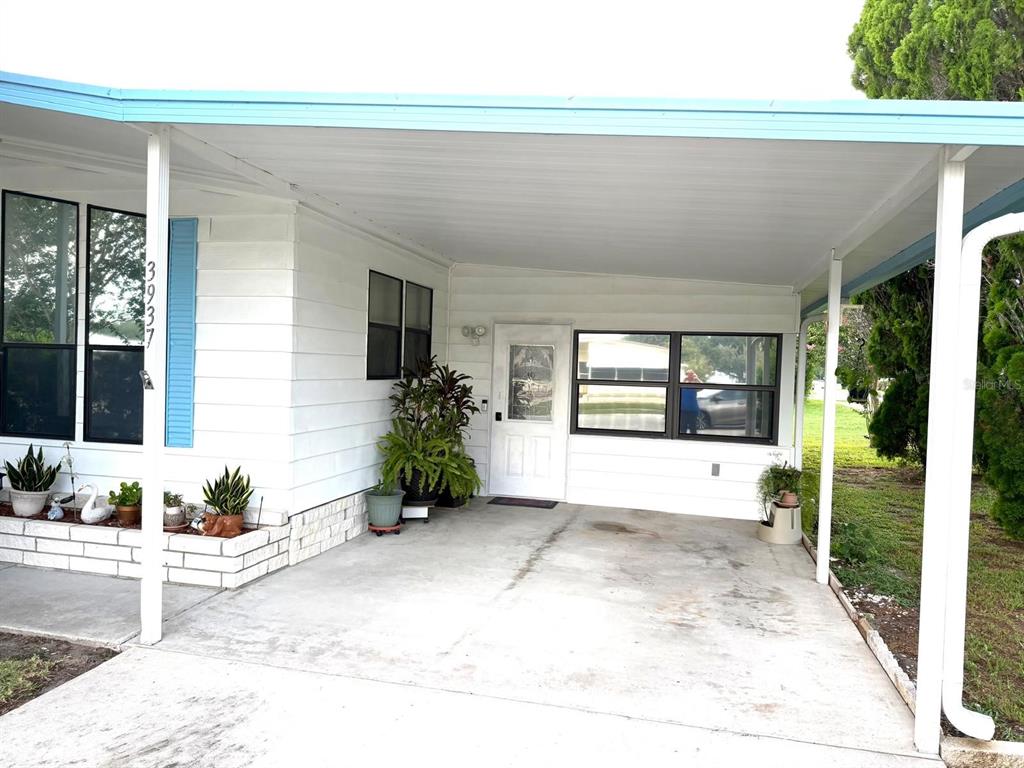 A white mobile home exterior features a concrete carport, a front door, and a brick planter — 3937 CHRIS DRIVE, WESLEY CHAPEL, FL