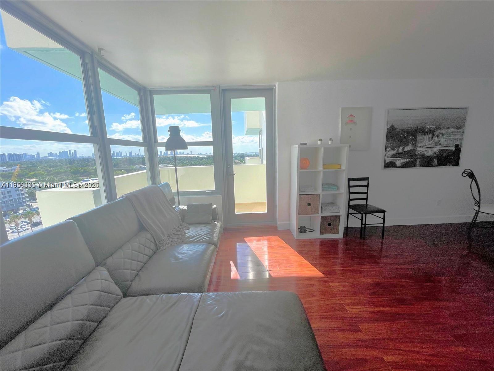 A living room features a grey sectional sofa, wood flooring, and a balcony with city views — 2899 Collins Ave # 1420, Miami Beach FL 33140, MIAMI BEACH, FL