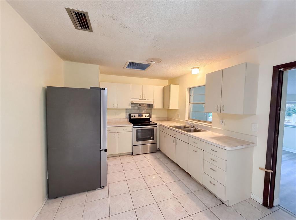 A kitchen with white cabinets, stainless steel appliances, and light-colored tile flooring — 722 VIRGINIA LANE, APOPKA, FL