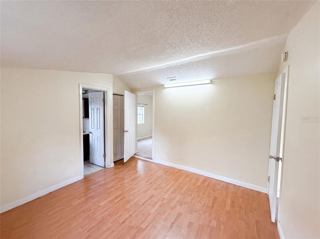 A room with light-colored walls, wood-look flooring, a fluorescent ceiling light, and multiple doorways — 722 VIRGINIA LANE, APOPKA, FL